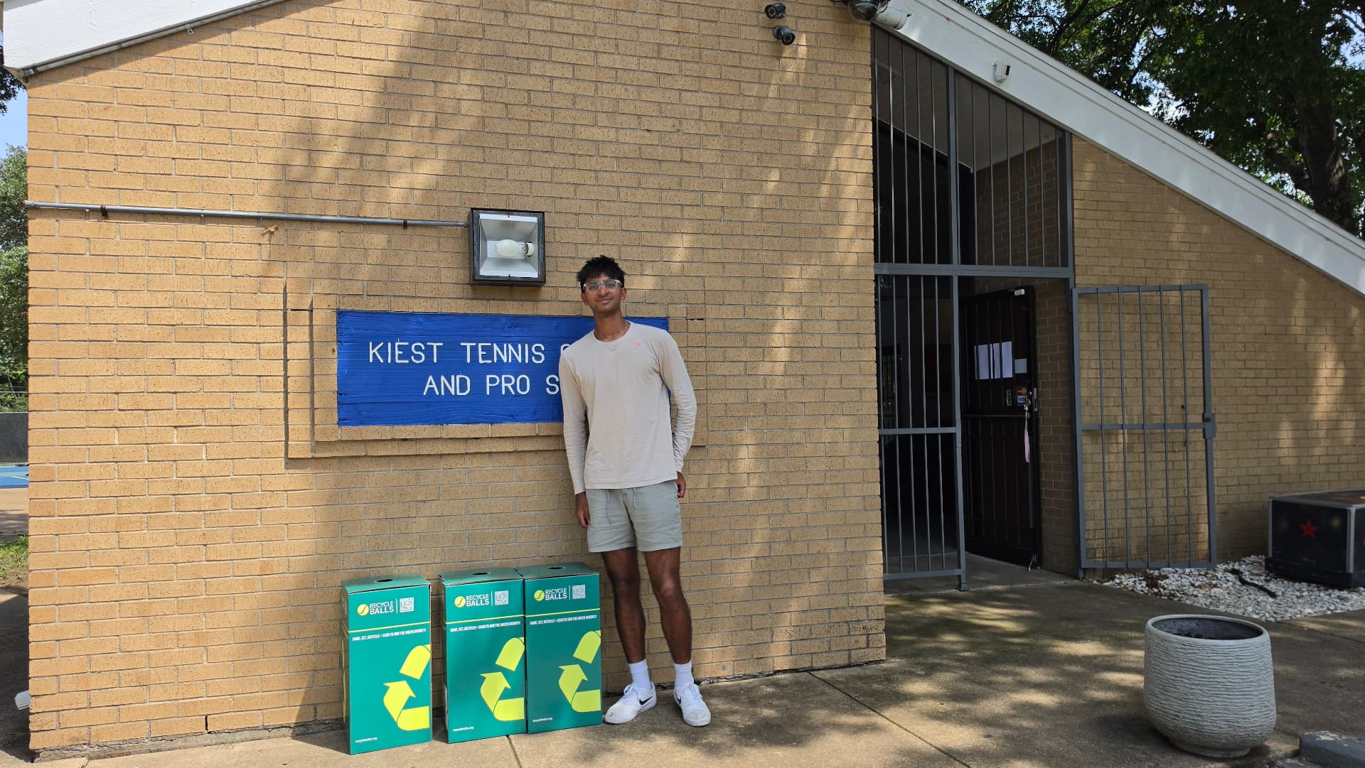 Prem Kamasani beside three green RecycleBalls collection bins at Kiest Tennis Center in Dallas