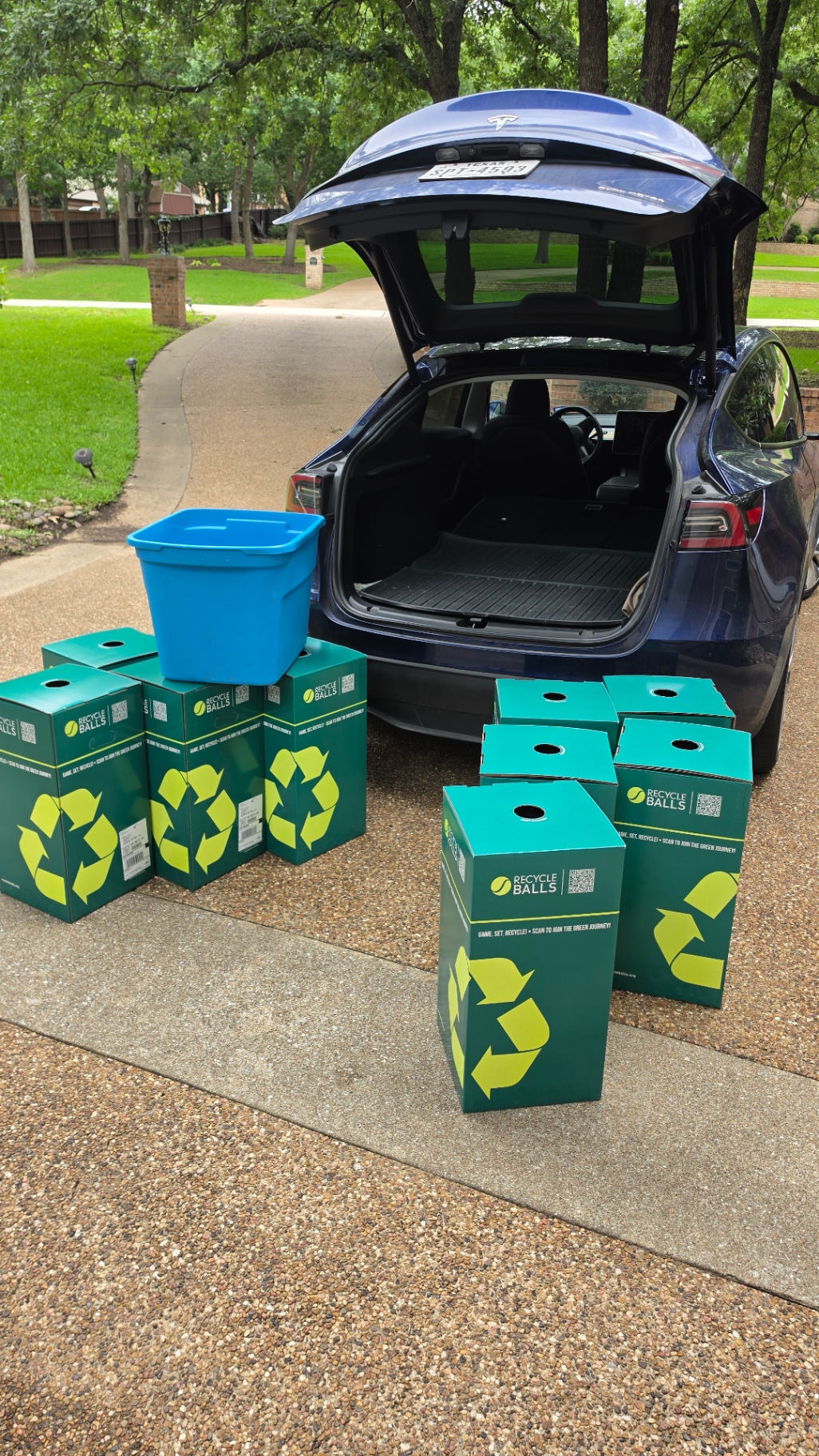 Eight RecycleBalls bins lined up in a driveway next to a Tesla ready for drop-off