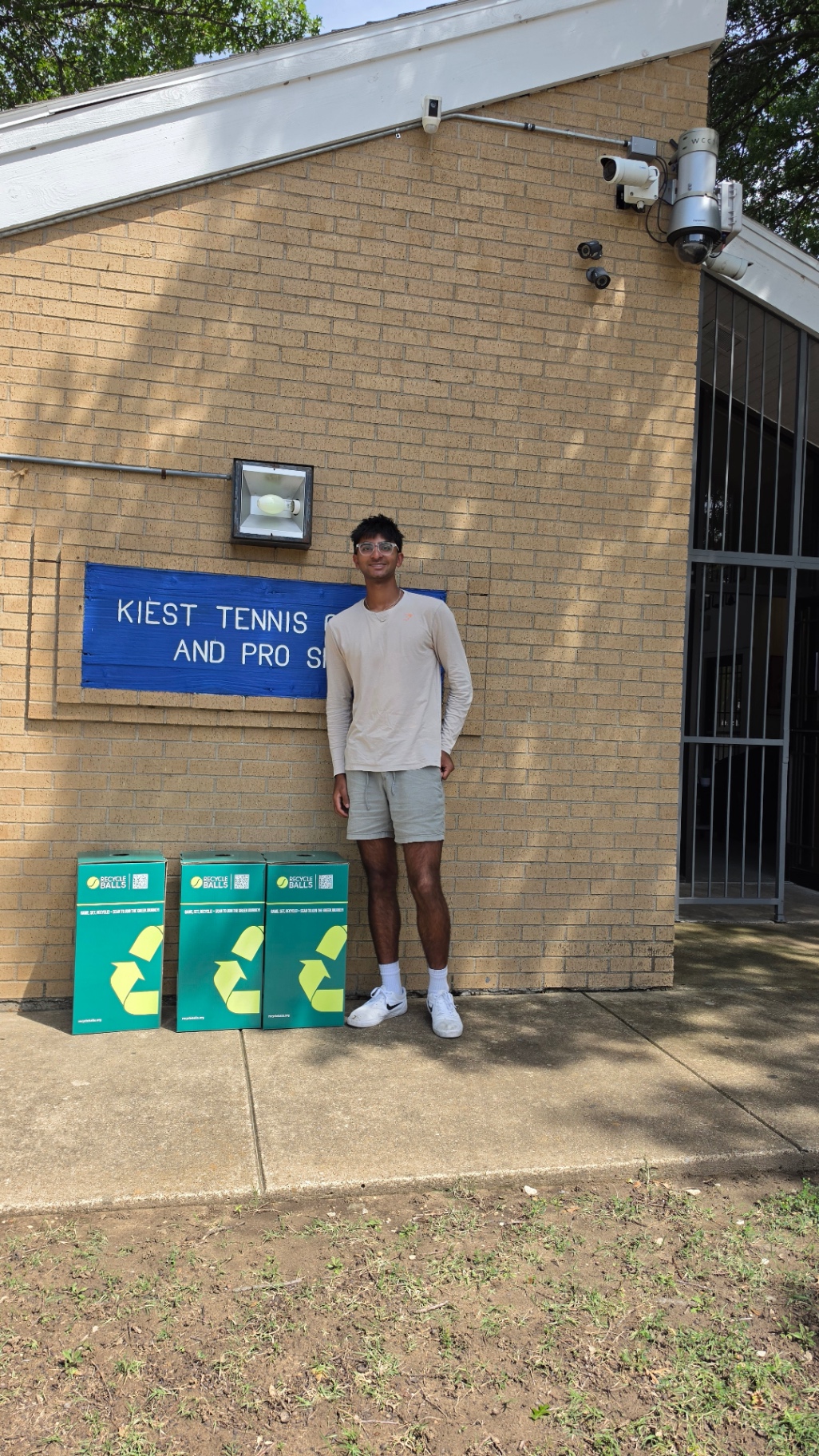 Prem standing next to three RecycleBalls bins at Kiest Tennis Center